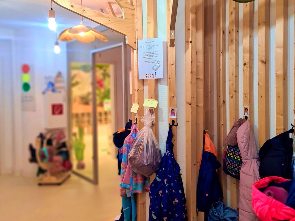 Kita Garderobe aus Holz mit bunten Kinderjacken und einem Elternaushang