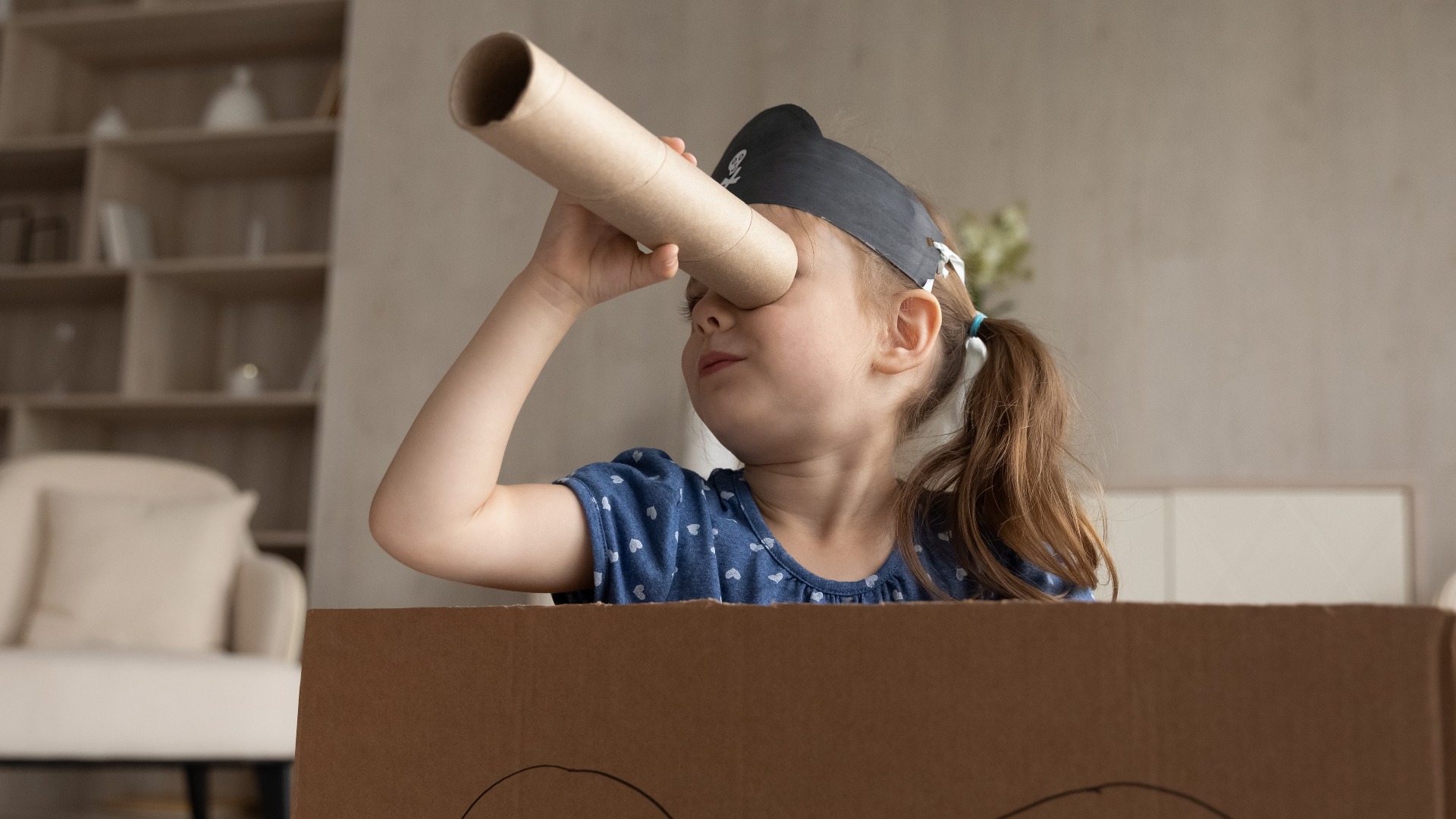Ein süßes, bezauberndes kleines Mädchen mit Piratenhut, das durch ein Fernglas schaut