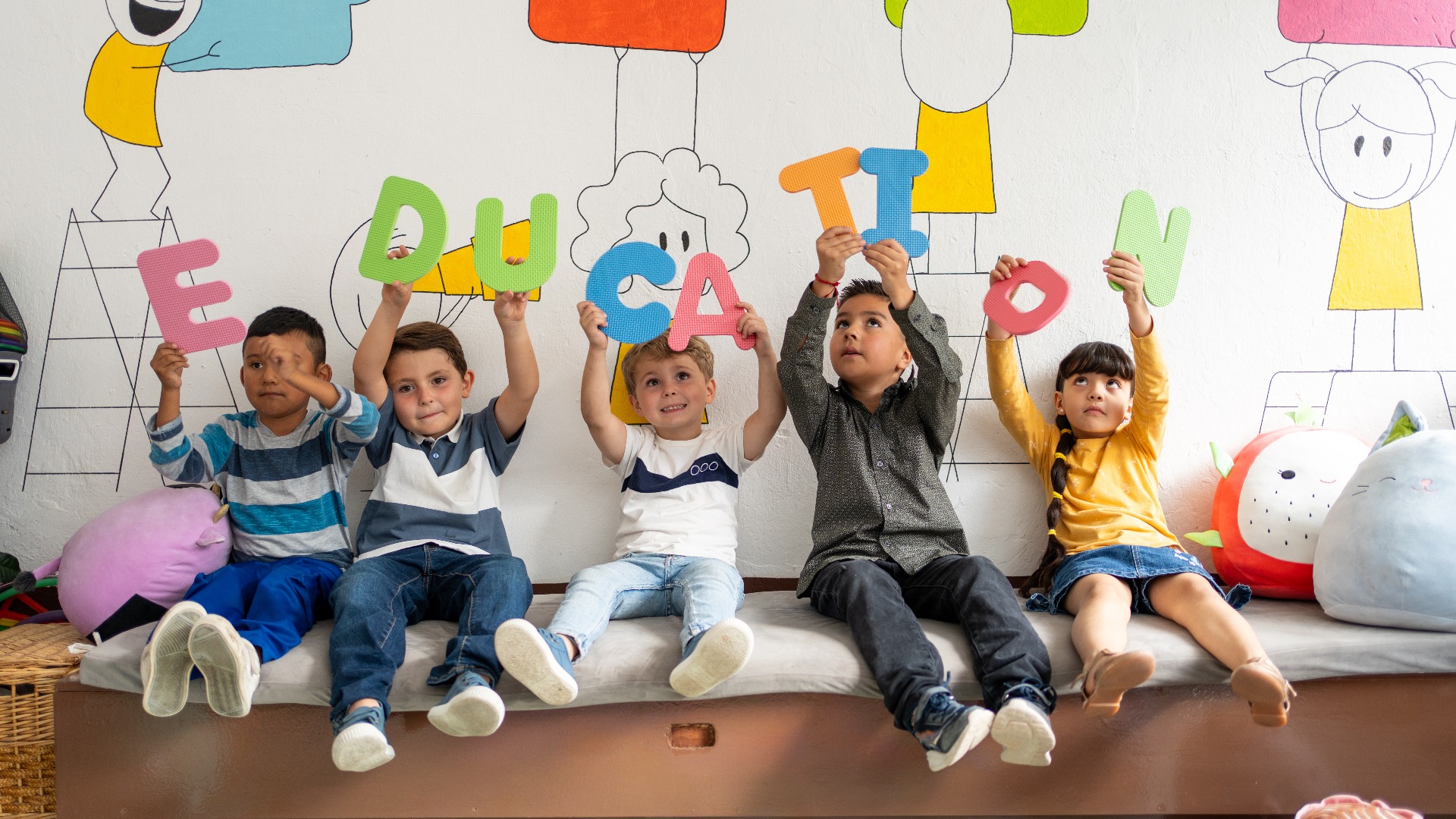 Eine bunte Gruppe von Vorschulkindern, die große, farbenfrohe Buchstaben hochhalten, aus denen sich das Wort „Bildung“ zusammensetzt, sitzt in einem hellen Klassenzimmer. Frühe Lese- und Schreibkompetenz, Vielfalt in der Bildung, Lernen im Kindergarten
