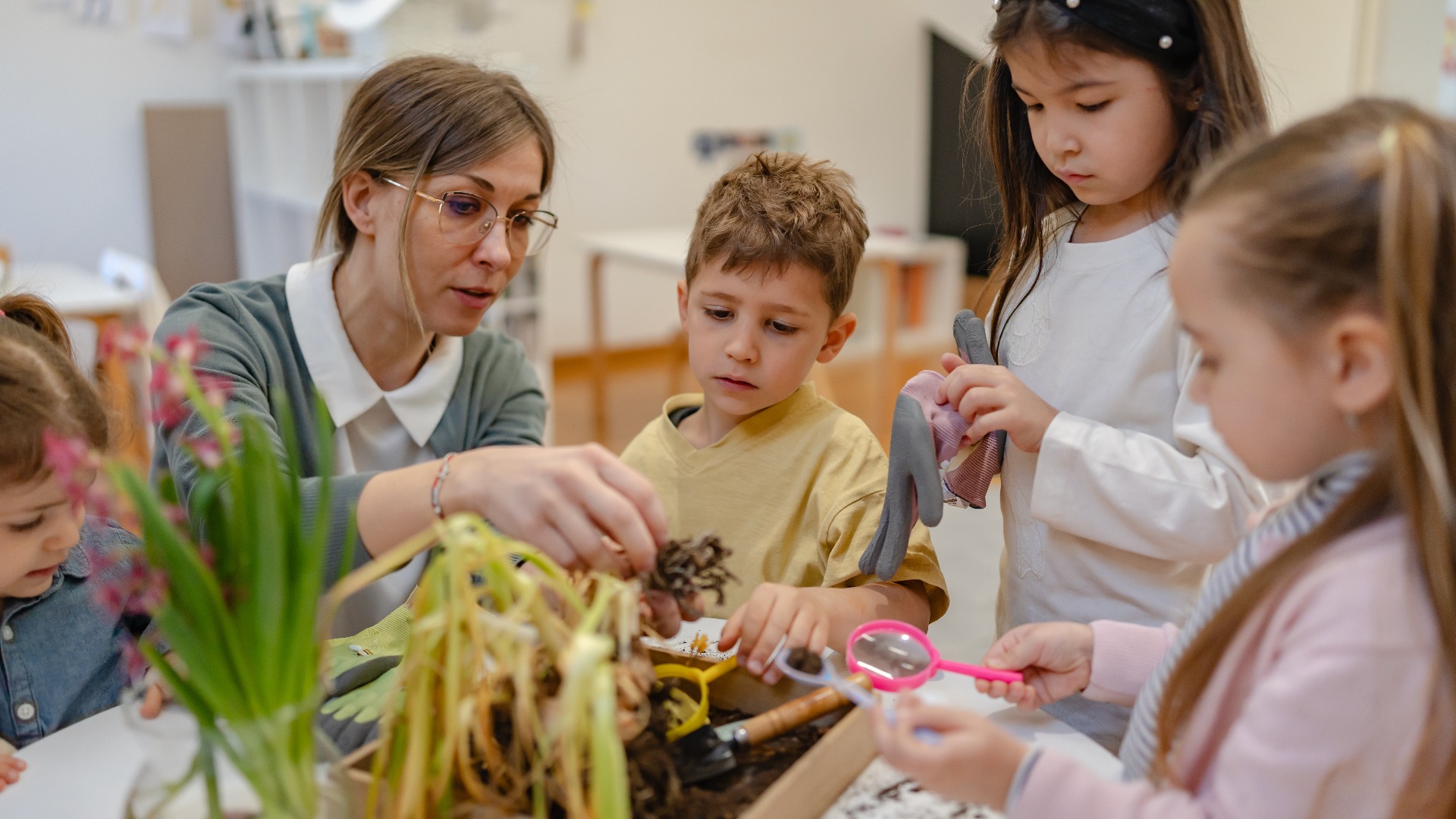 Eine Lehrkraft und neugierige Kinder beschäftigen sich im Rahmen einer naturwissenschaftlichen Unterrichtsaktivität mit Boden und Pflanzen und fördern so das praxisorientierte Lernen und das Umweltbewusstsein in einer vielfältigen Schülergruppe.